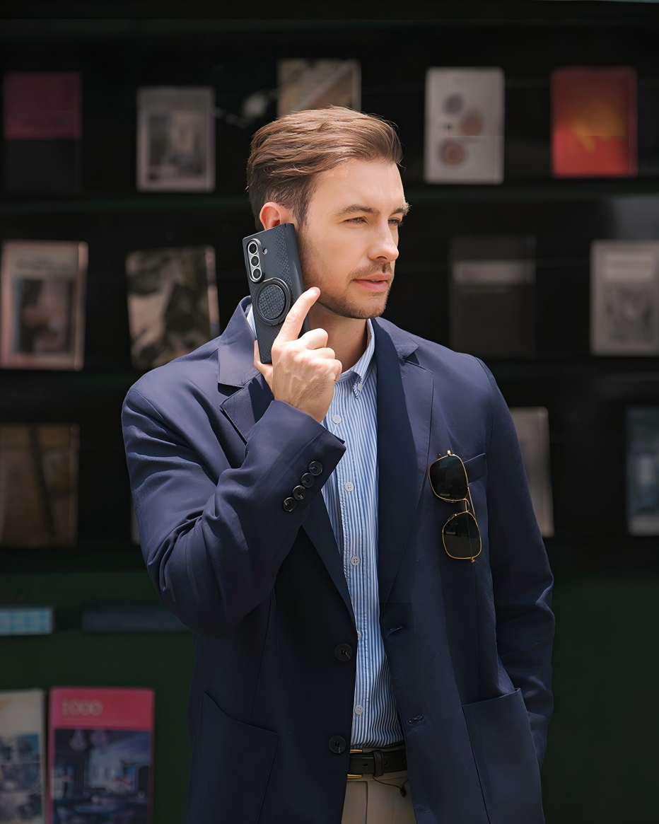 A man in a navy blazer and light blue striped shirt holds a black ARMORGRID Z Fold 8 Ultra smartphone to his ear, standing in front of a dark display wall with framed pictures. The text 'ARMORGRID Z Fold 8 Ultra' is visible at the bottom left.